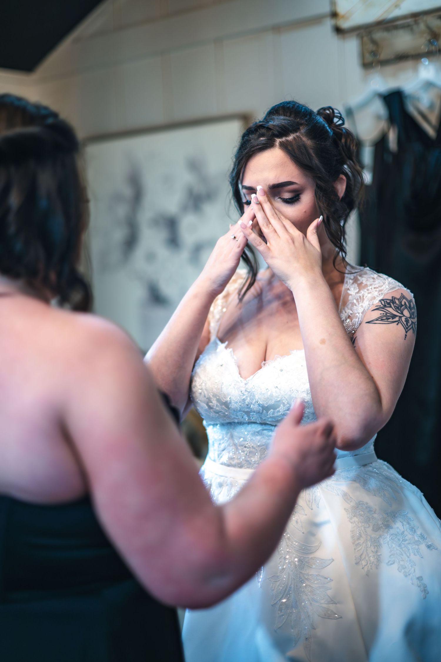 Bride wearing white lace wedding dress covers face with hands in emotional moment during wedding preparations.