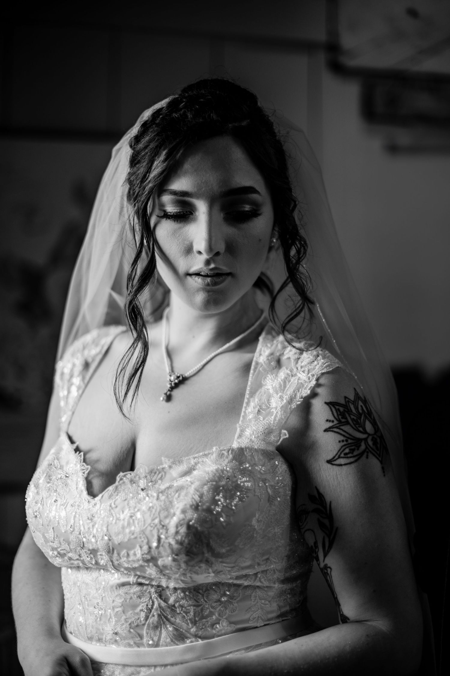 A bride in a white lace wedding dress with a floral tattoo on her arm poses in black and white portrait.