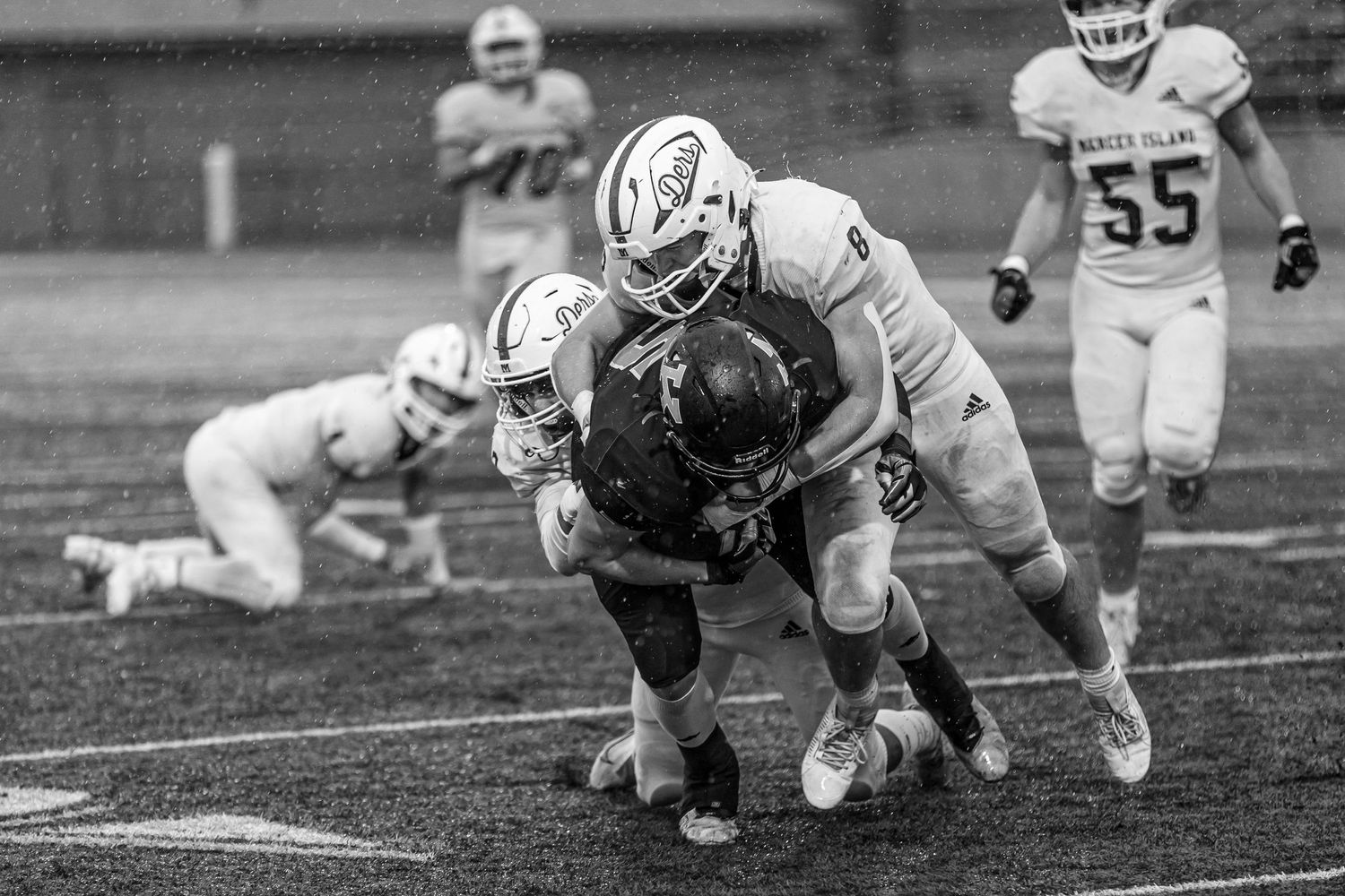 Black and white action shot of football players tackling during a game.