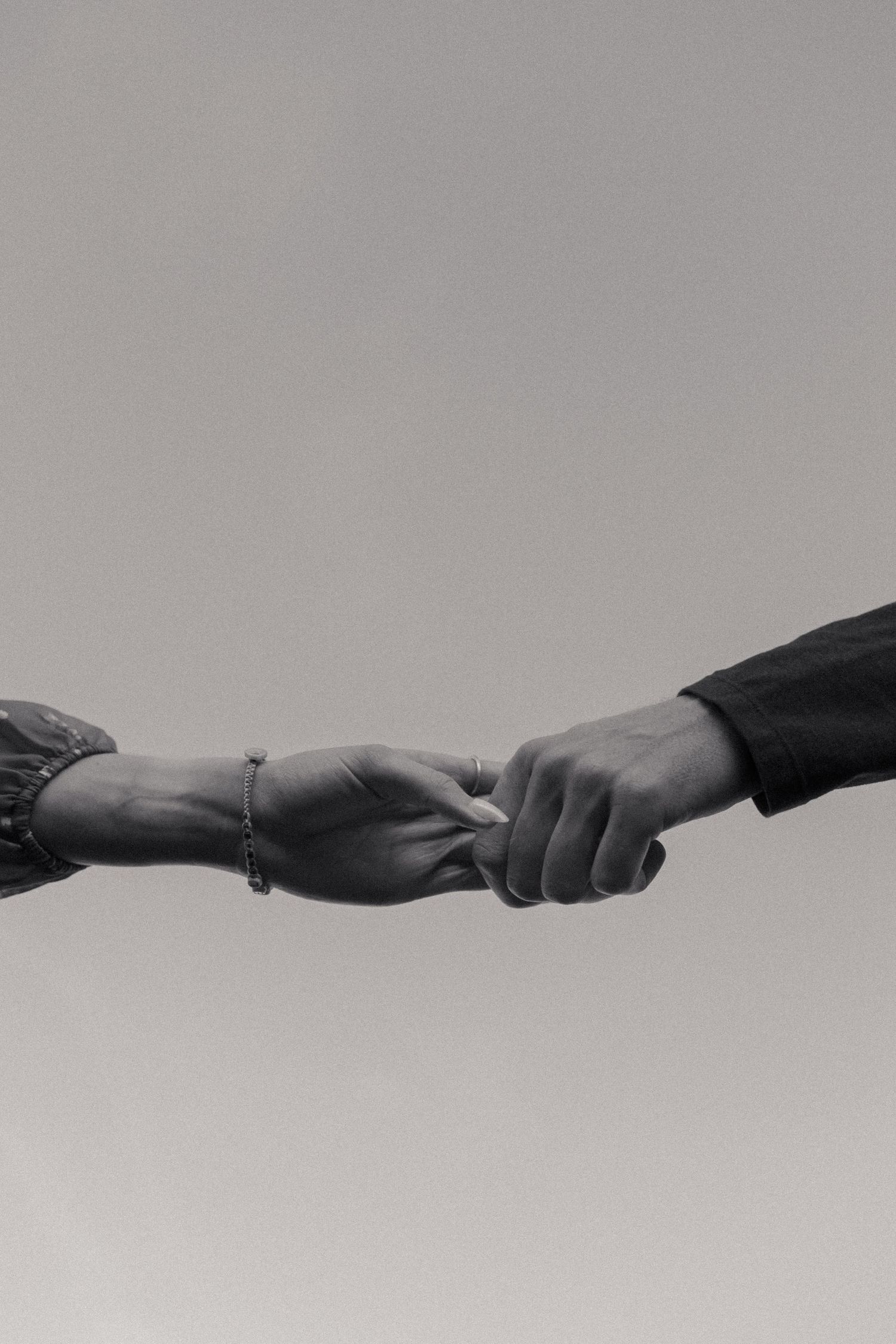 Black and white close-up of two hands reaching to hold each other against grey sky.