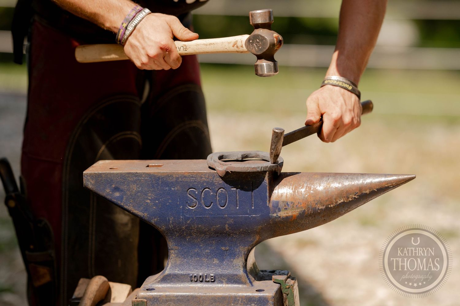 Hands working with hammers on a Scout anvil during metalworking.