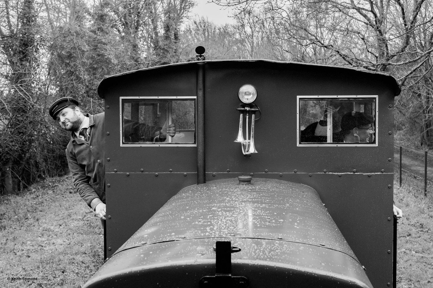 Vintage black and white photo of a railway train engine car with two square windows and decorative wind chimes.