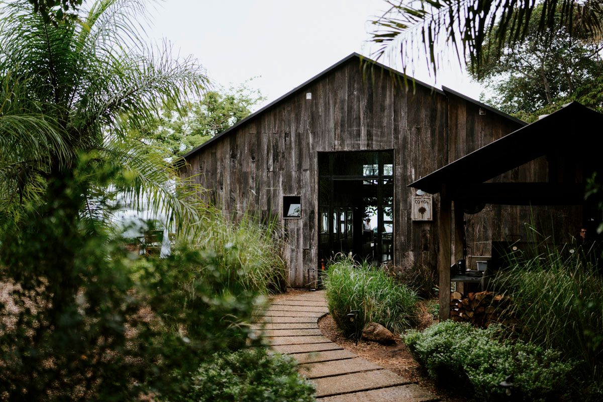 Rustic wooden barn with boardwalk entrance surrounded by tropical plants and palms.