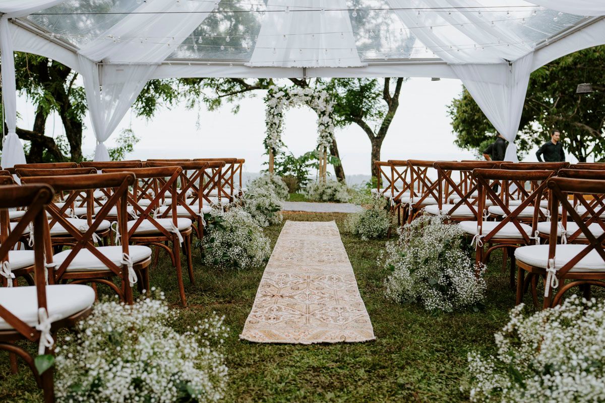 White tent setup for outdoor wedding with wooden chairs and floral decorations.