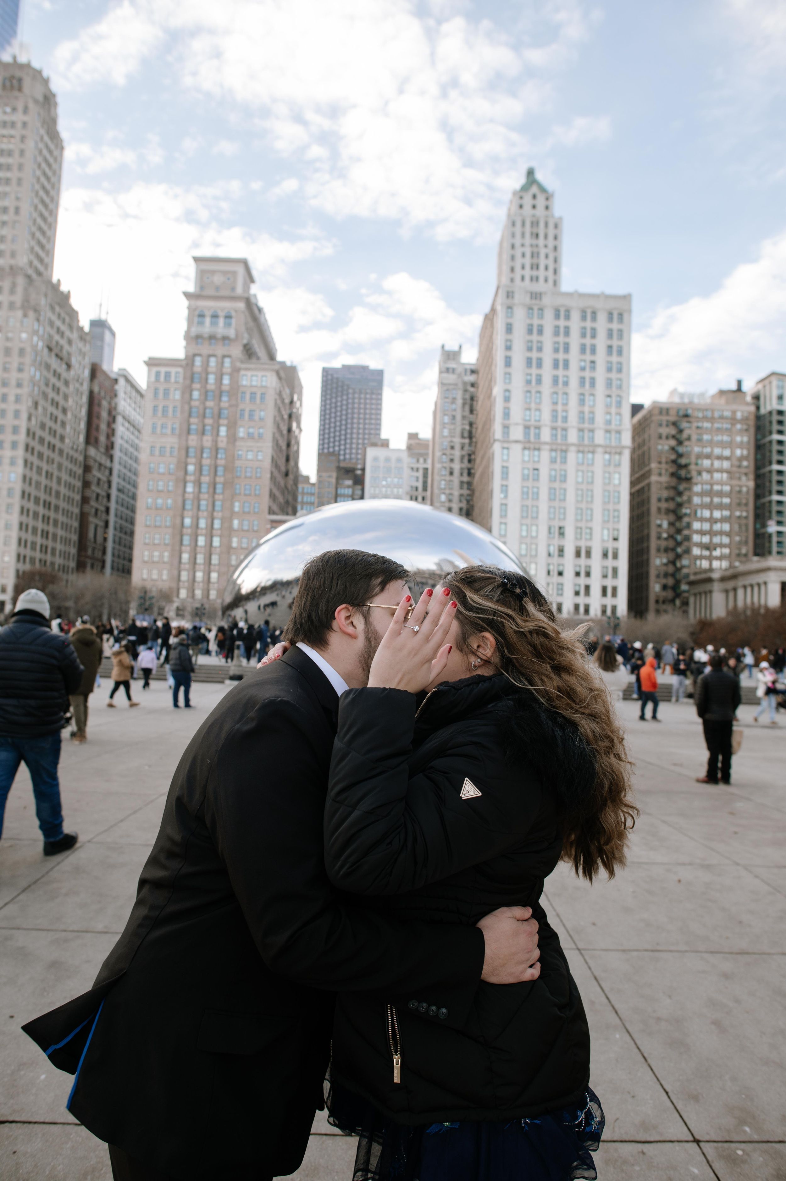 Two people share an intimate moment in front of Cloud Gate sculpture in Chicago's Millennium Park.