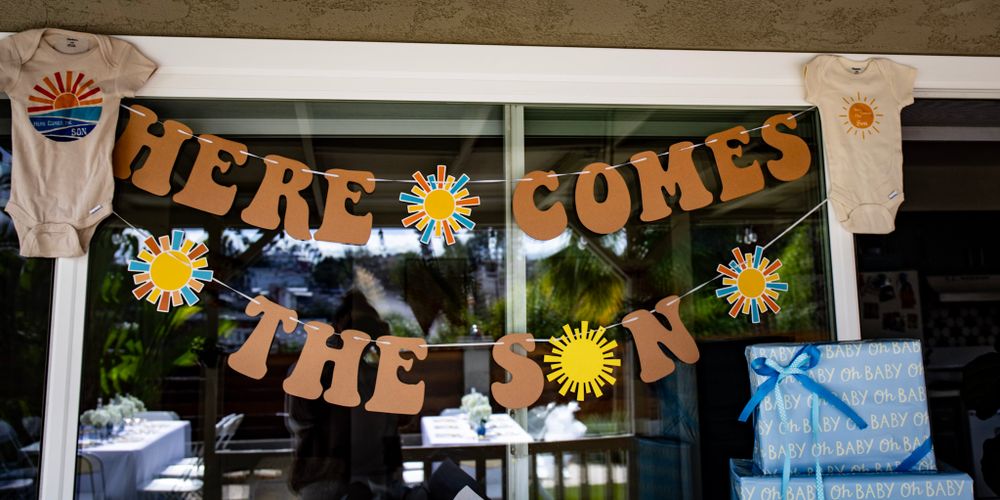 Here Comes The Sun banner with paper daisies decorating a baby shower venue.
