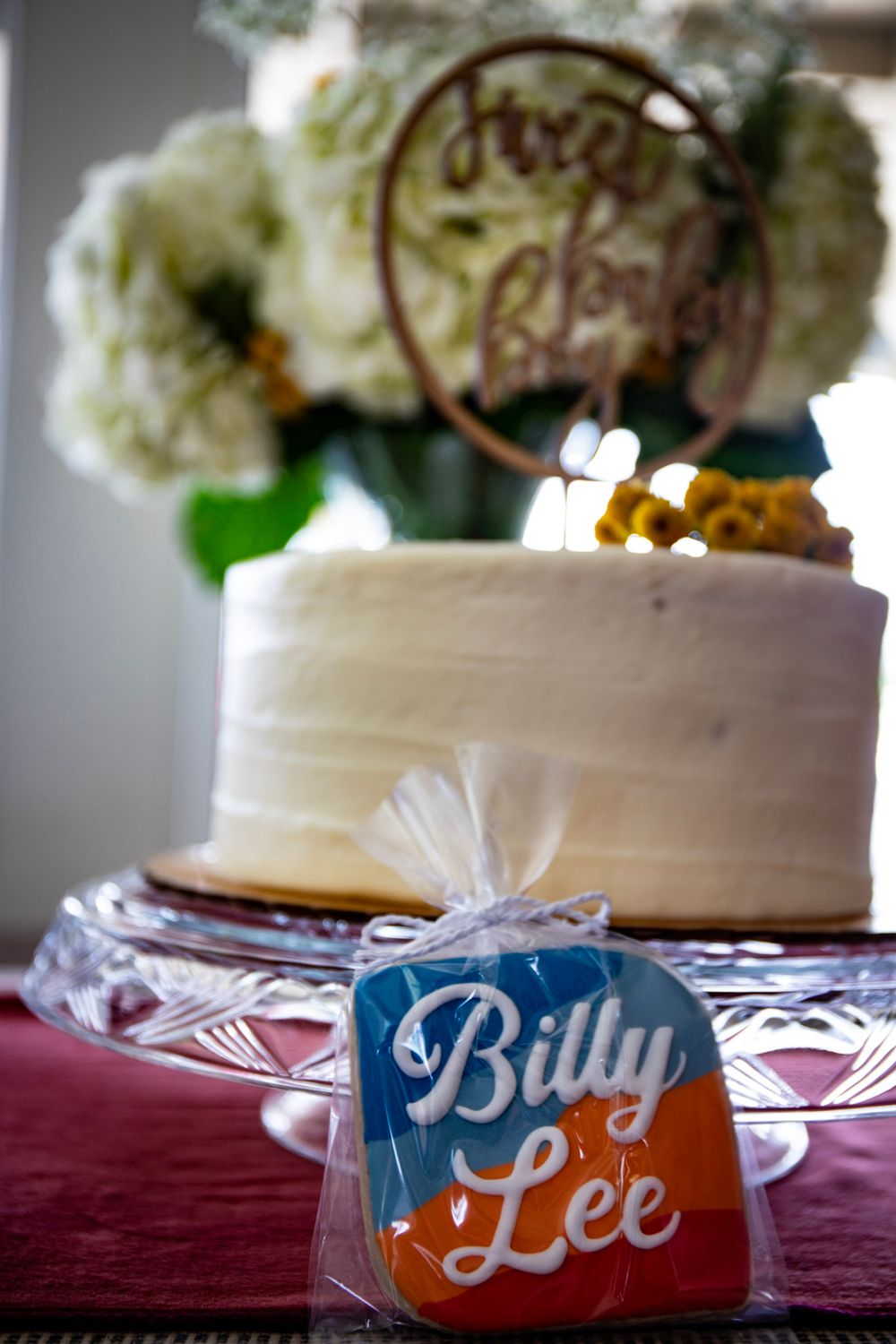 White frosted cake with Billy Lee branded cookies and floral decorations.