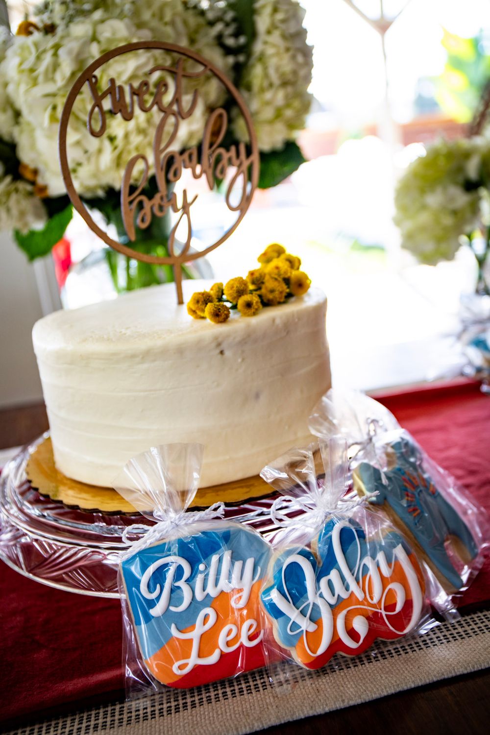 Close-up of white celebration cake with gold topper and decorated cookies.