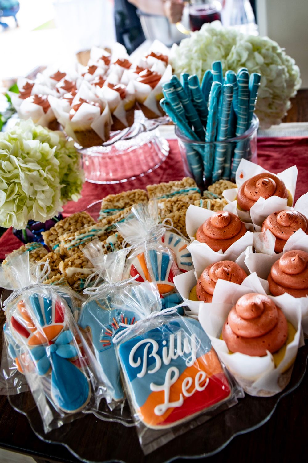 Dessert table with decorated cookies, cupcakes, and hydrangea flowers at a baby shower event.