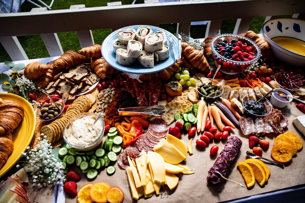 Overhead view of an abundant charcuterie board with croissants, fruits, meats and cheeses on wooden surface.