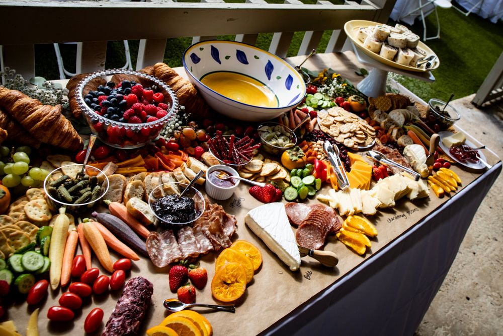 Gourmet appetizer spread featuring charcuterie, fresh fruits, nuts and dips arranged on dark tablecloth.