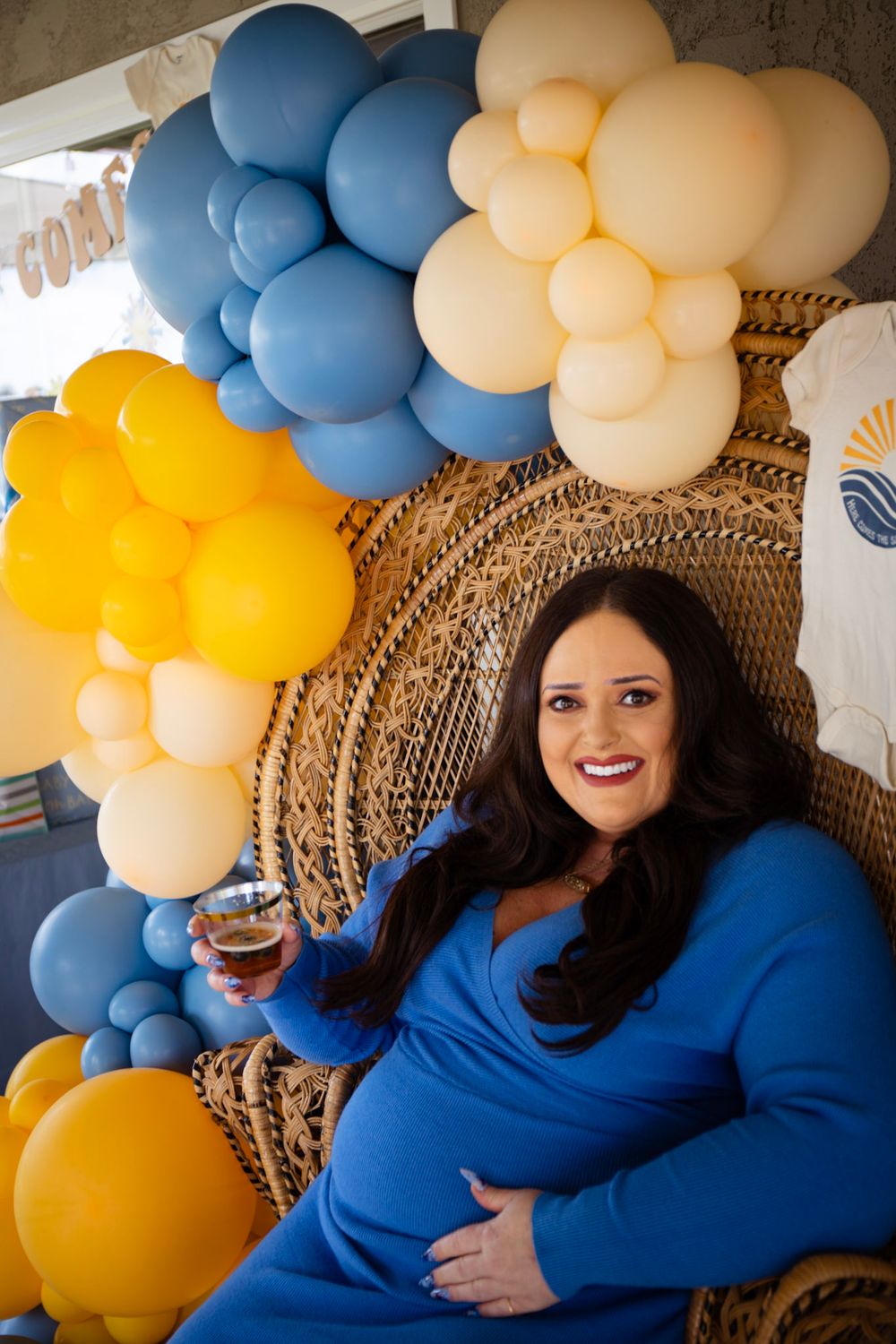 Festive balloon arch installation in blue, yellow and cream colors with woven peacock chair.