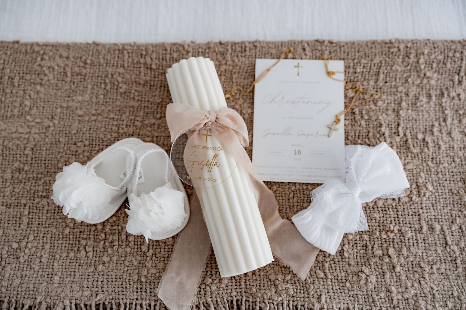White candle wrapped with neutral ribbon sits on rustic fabric alongside delicate feminine decor and cards.
