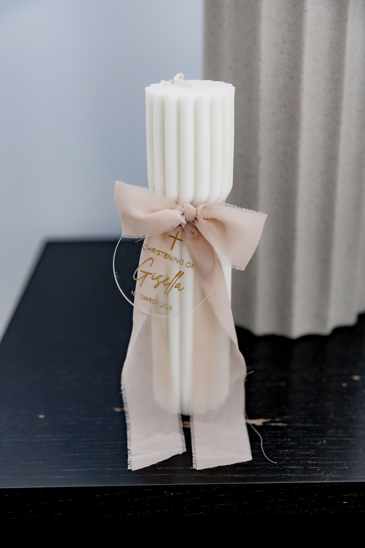 White fluted candle decorated with a pale pink bow and gold tag for a christening ceremony.