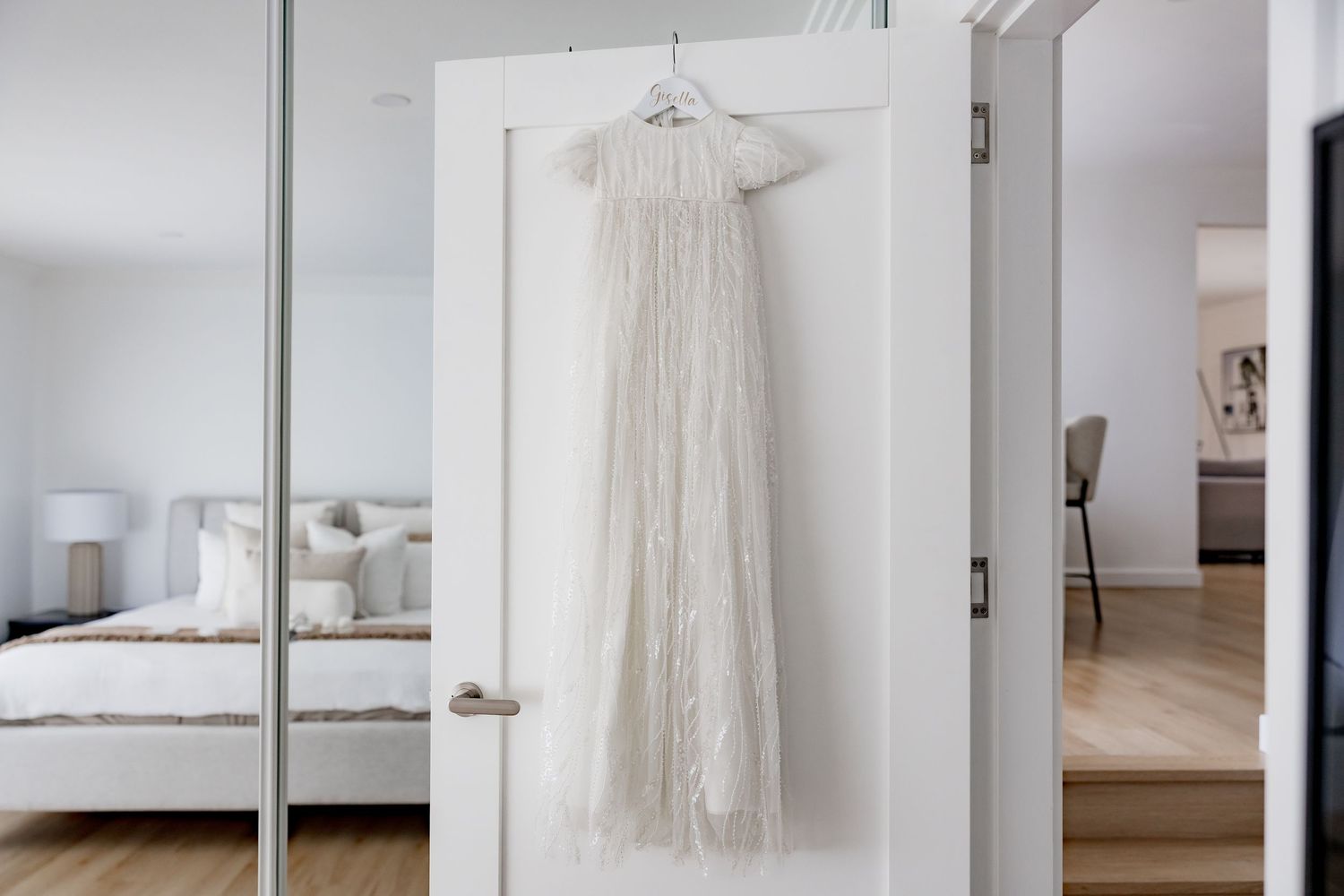 White lace christening gown hanging on door in bright minimalist bedroom interior.