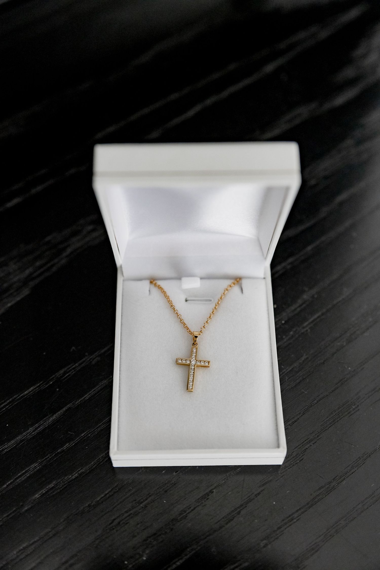 Gold cross necklace pendant displayed in a white jewelry box.