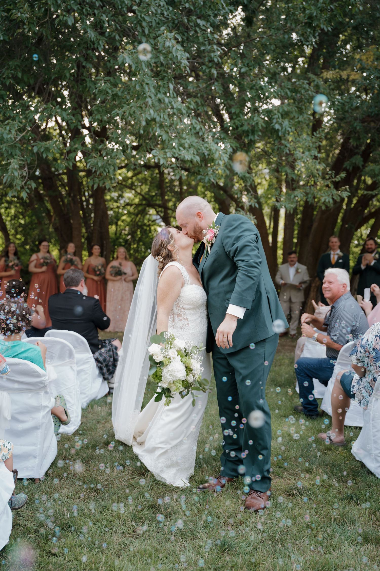 Romantic wedding couple dips and kisses in garden setting with confetti floating through the air at outdoor ceremony.