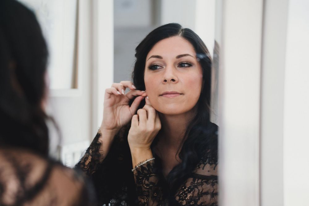 Woman with dark hair applies makeup while looking in mirror reflection.