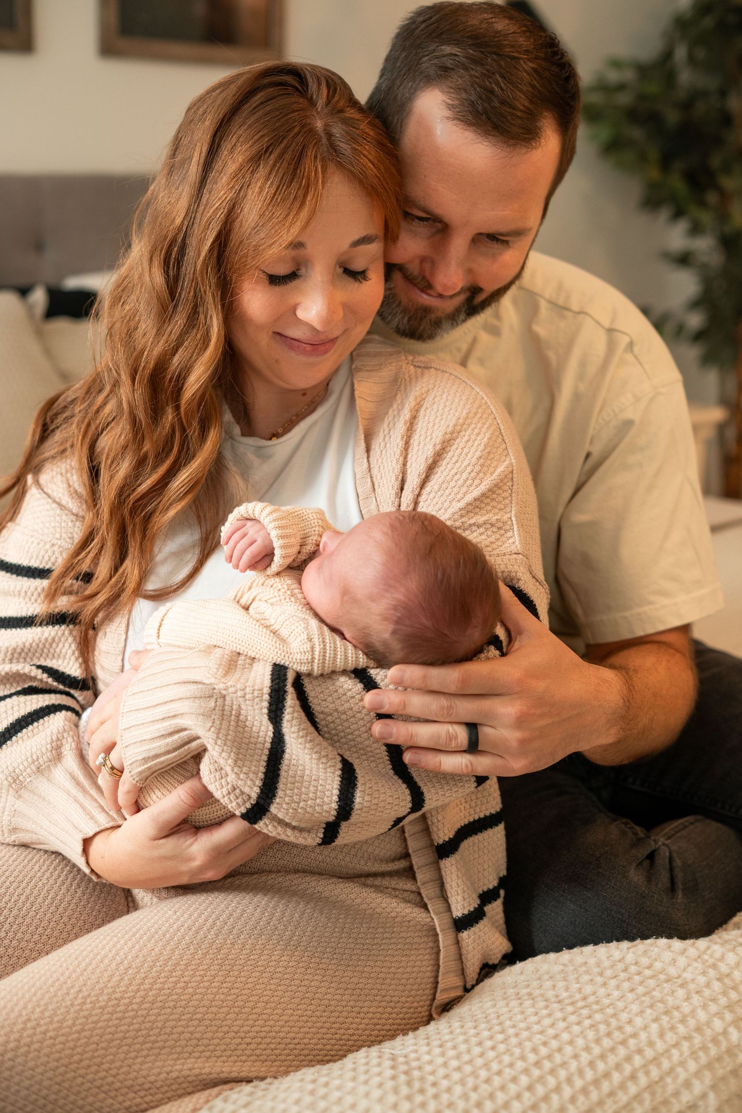 A couple in cozy sweaters lovingly cradles their newborn baby while sitting together on a sofa.