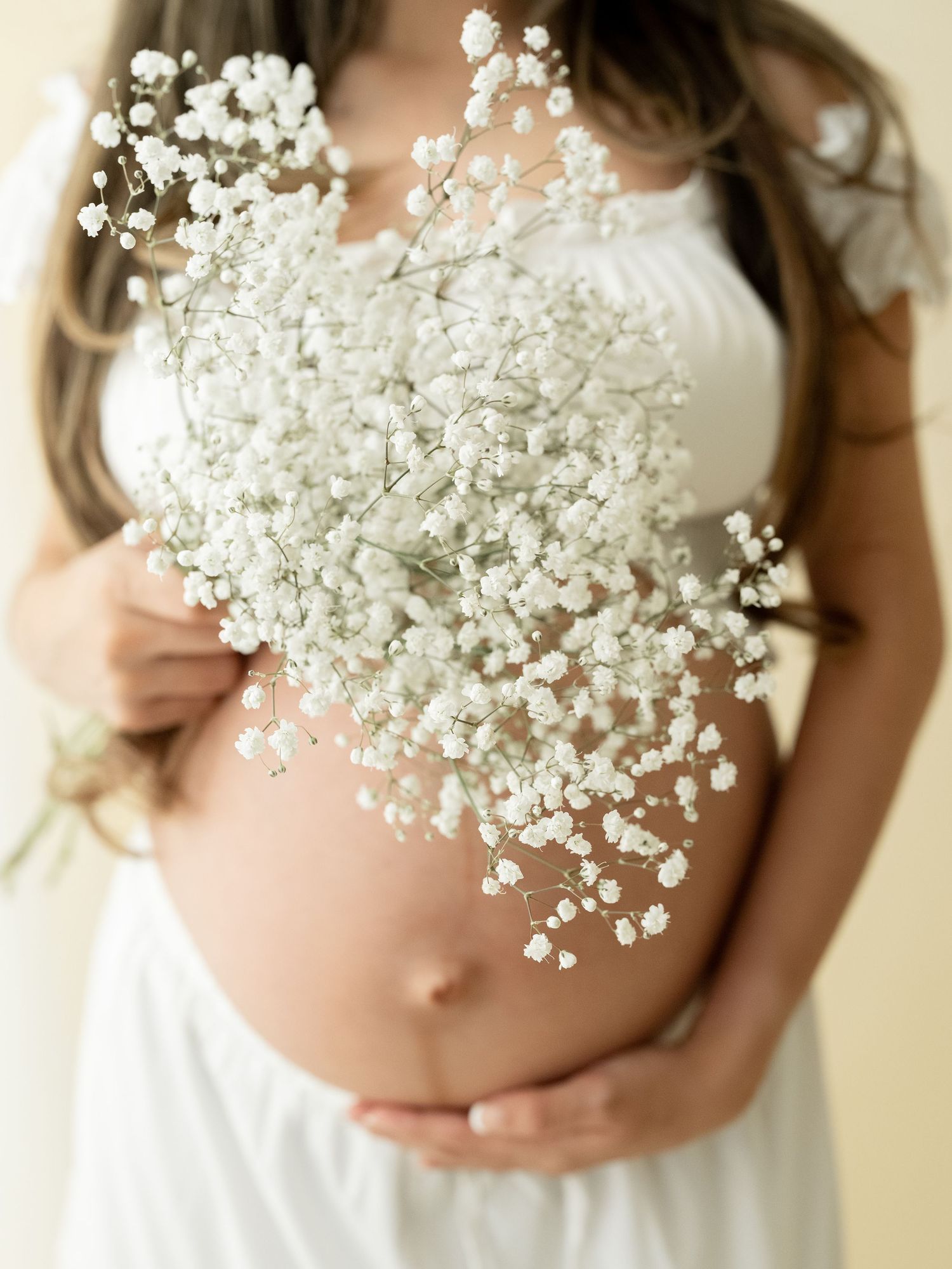 A sleeping newborn baby swaddled in soft white fabric sleeps peacefully against a light neutral background.