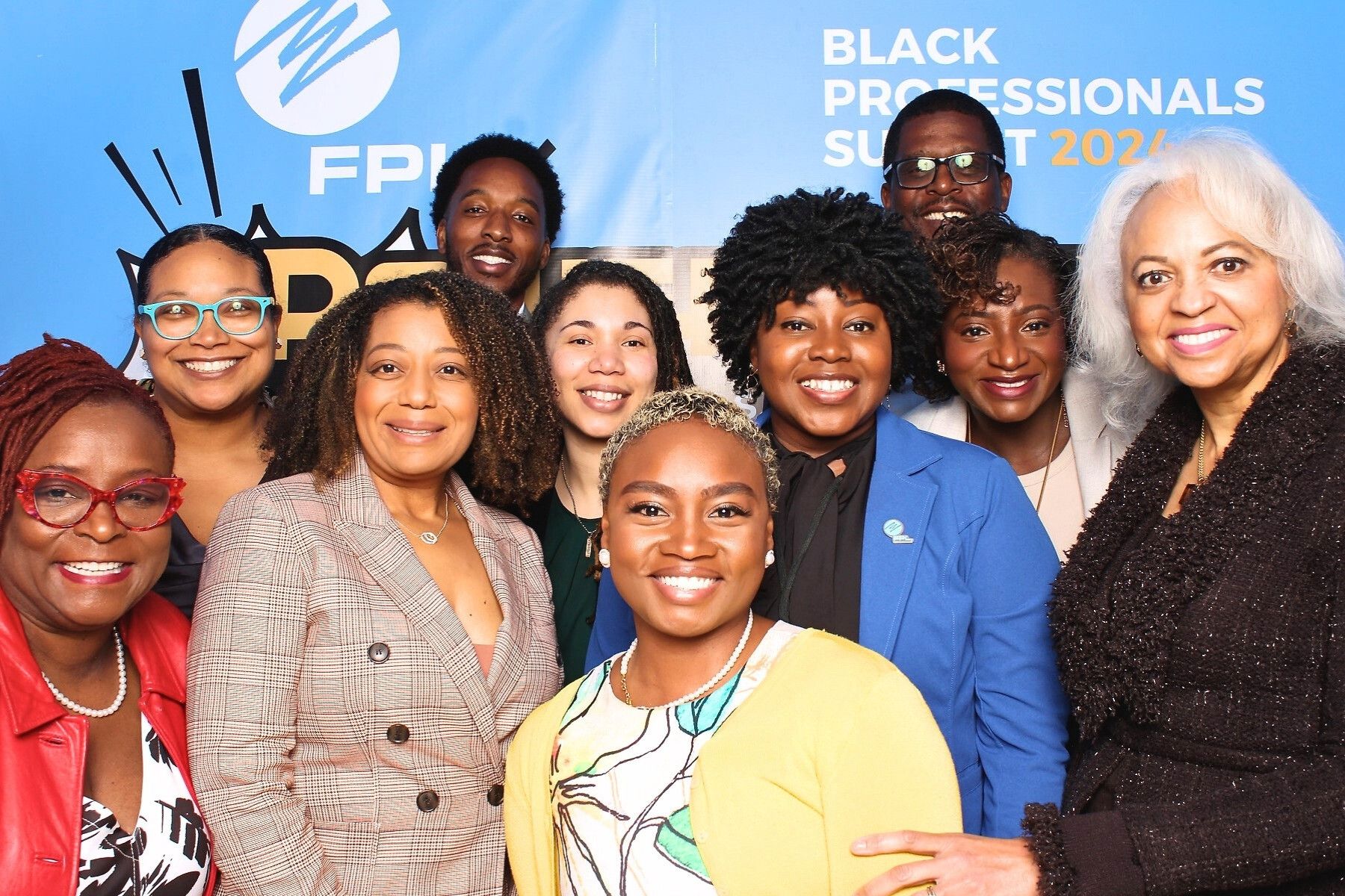 A group of professionals pose together at a business event with a blue banner visible in the background.
