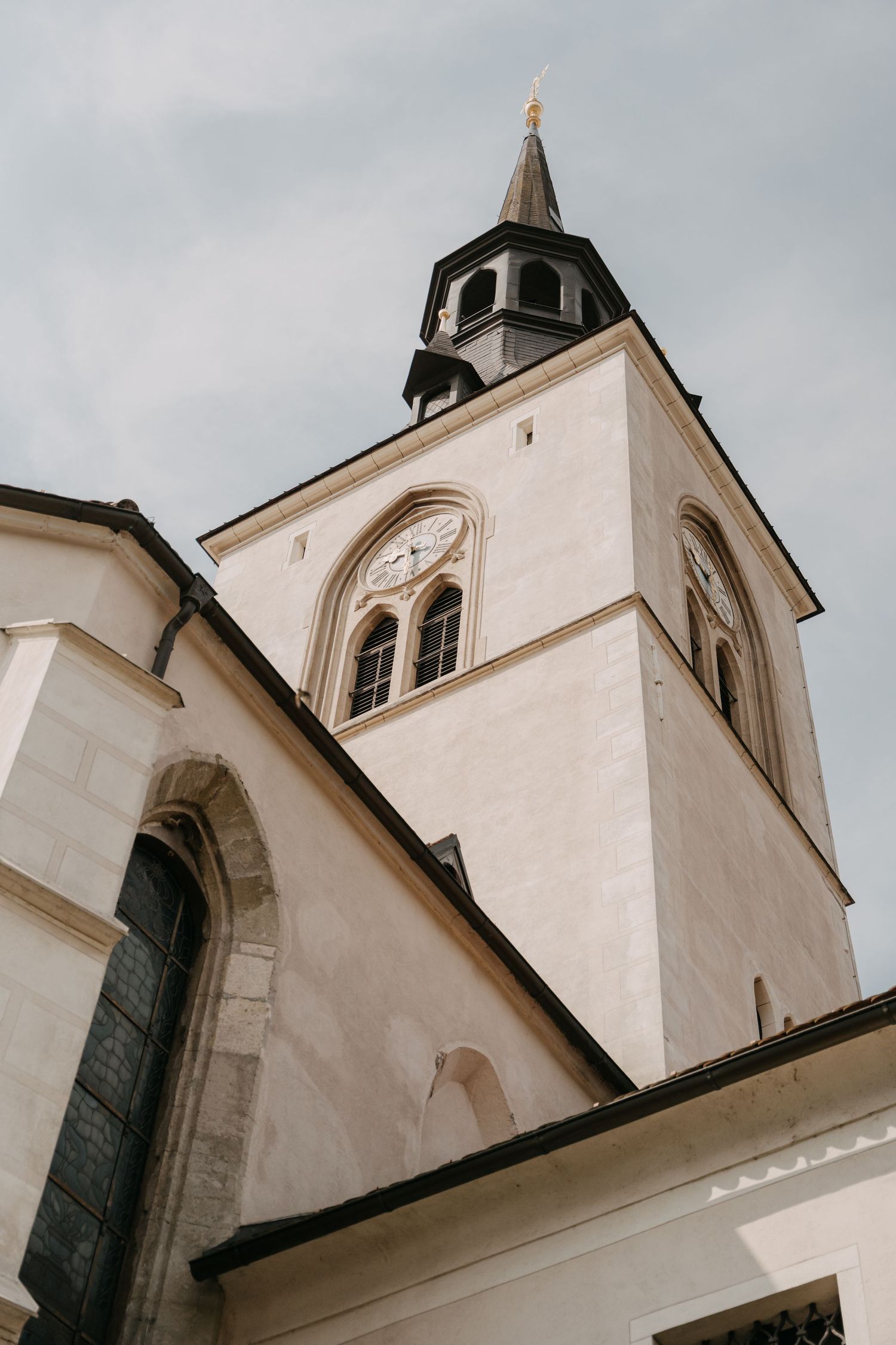 Low angle view of a white church steeple with clock face and pointed spire against cloudy sky.