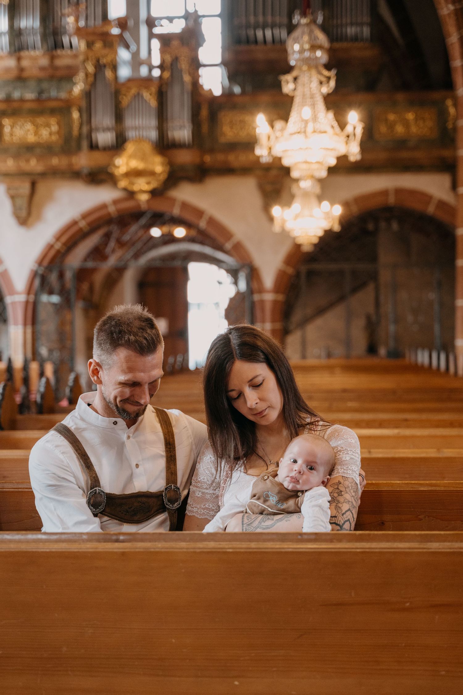 A family sits together in a church pew under ornate chandeliers and decorative architecture.