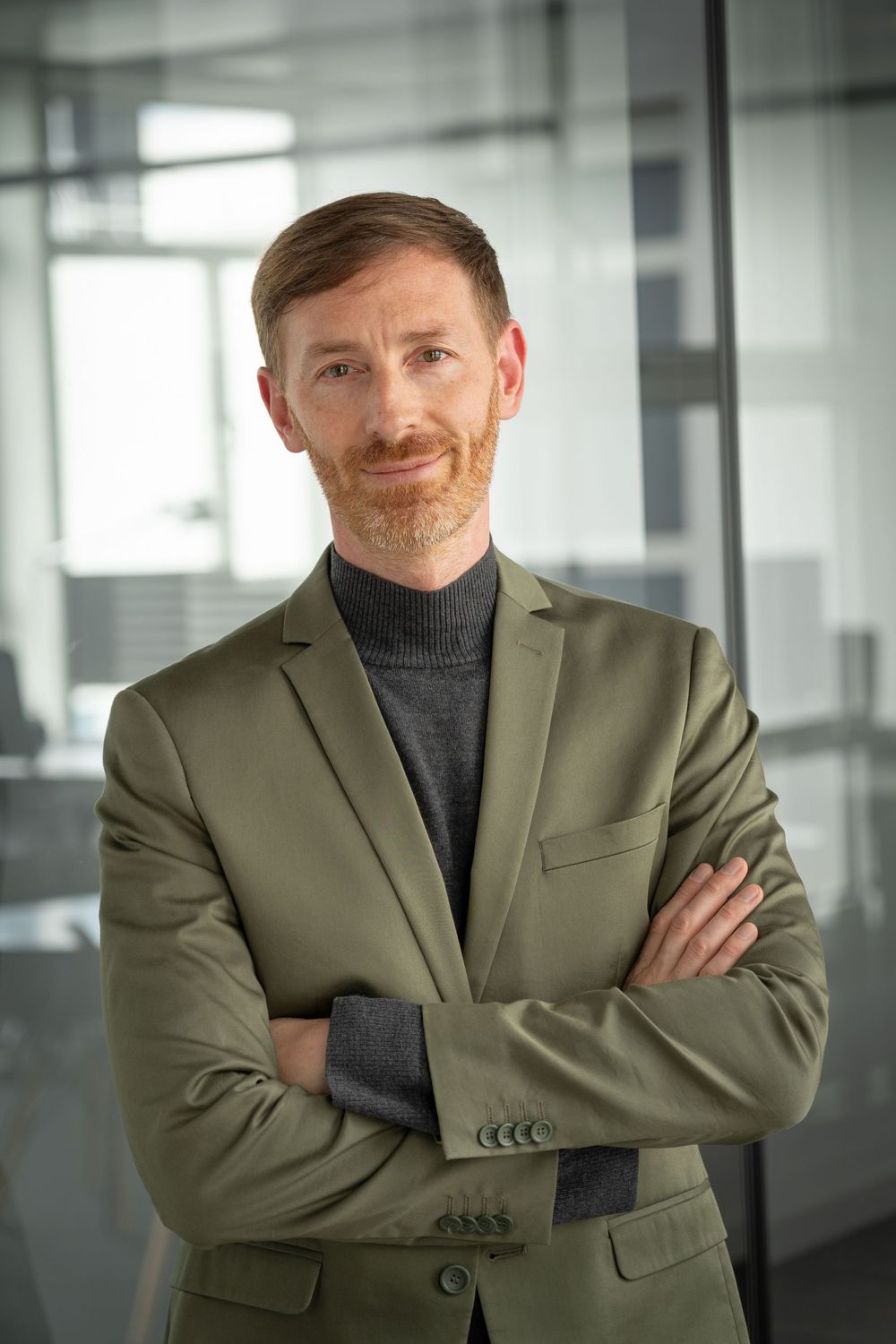 Professional wearing olive green blazer and turtleneck in modern office setting.