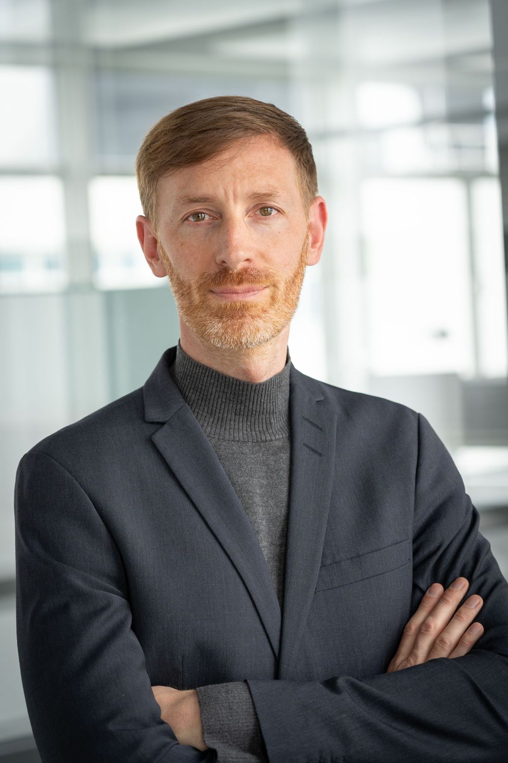 Business professional in navy blazer and turtleneck against office windows.