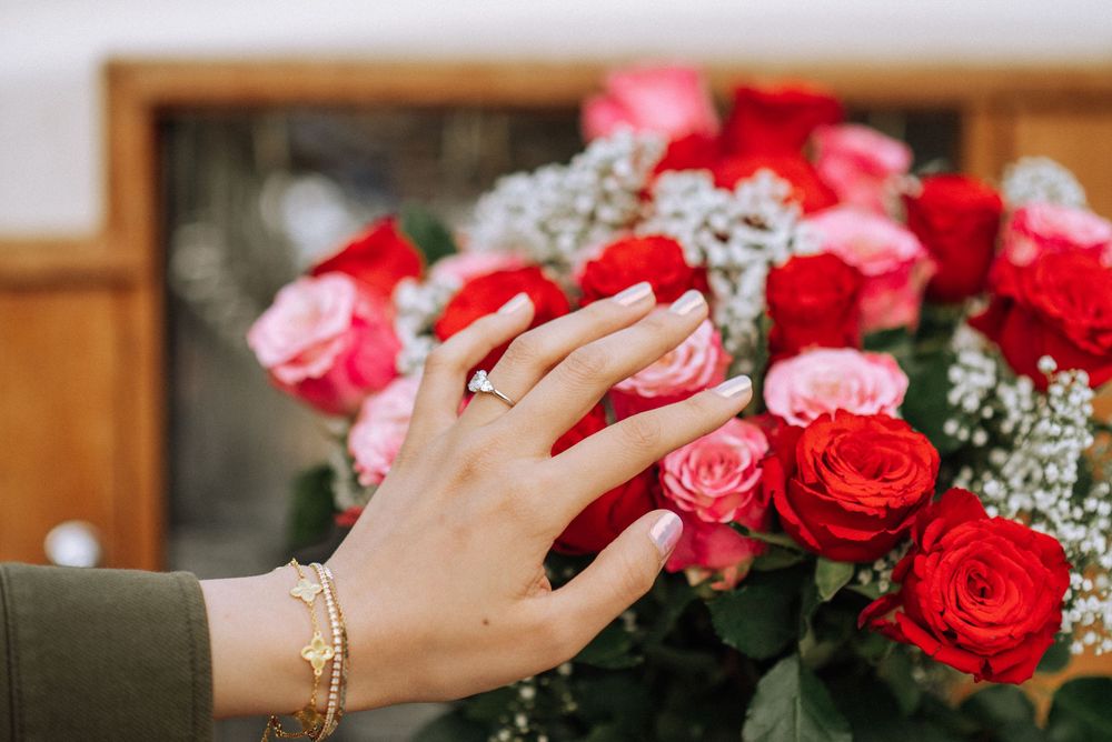 Close-up of hands touching near pink and red roses with baby's breath flowers.