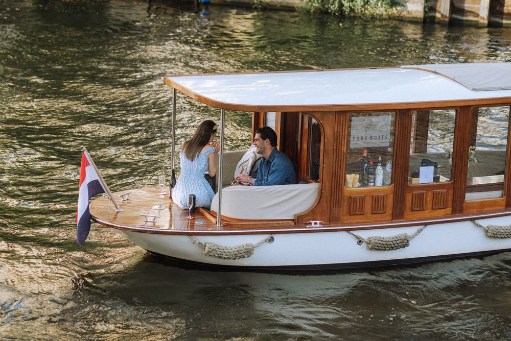 Wooden tour boat cruising through Amsterdam canal on sunny day.