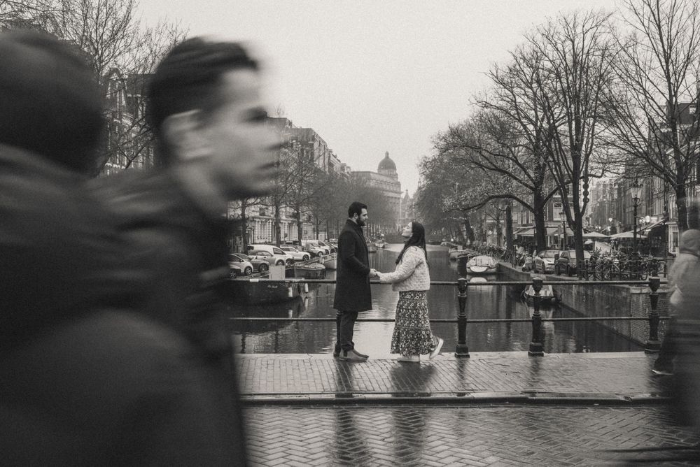 Black and white street scene in Amsterdam with people walking near canals.