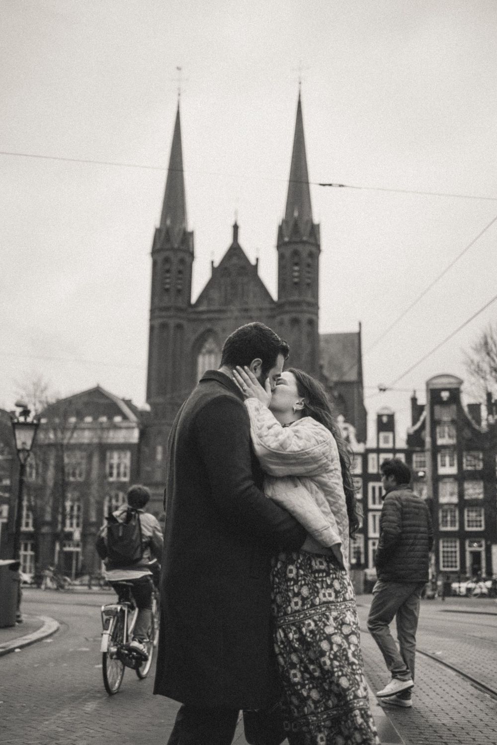 Vintage black and white photo of a couple embracing near a Gothic cathedral in Amsterdam.