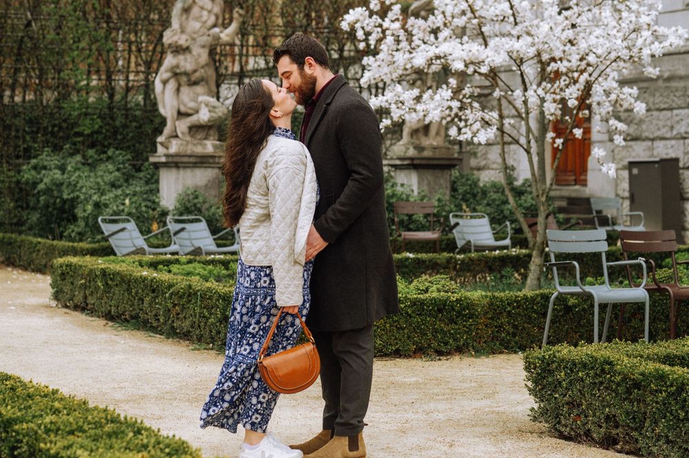 Couple walking and embracing in a manicured garden with stone walls and benches.