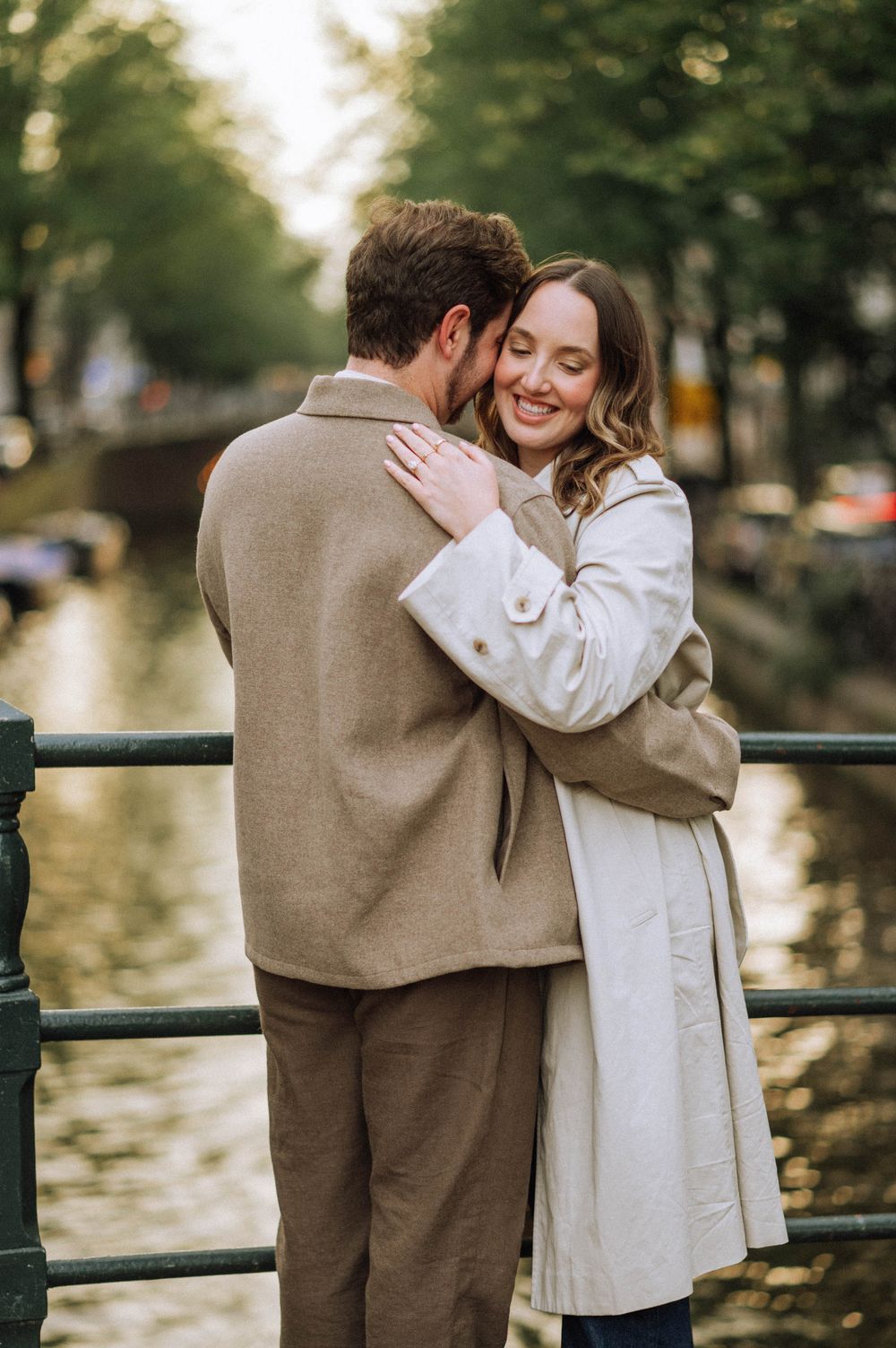 Intimate couple embracing by canal railing during golden hour in Amsterdam.