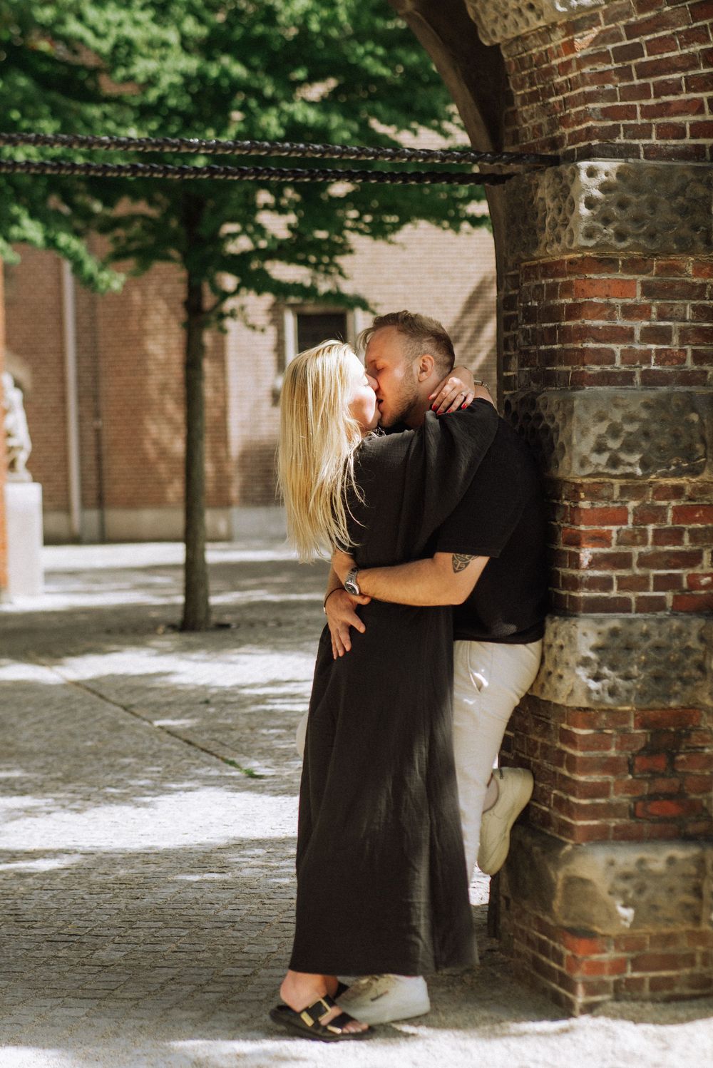 Two figures sharing an intimate moment against a brick wall background.