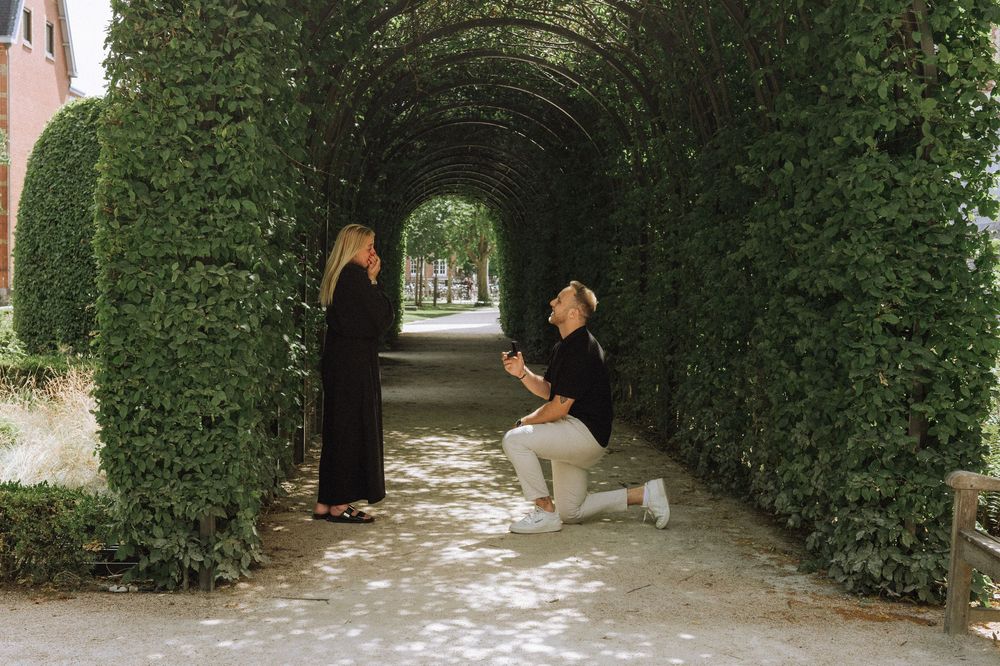 A couple embracing in a garden pathway lined with green hedges and brick walls.