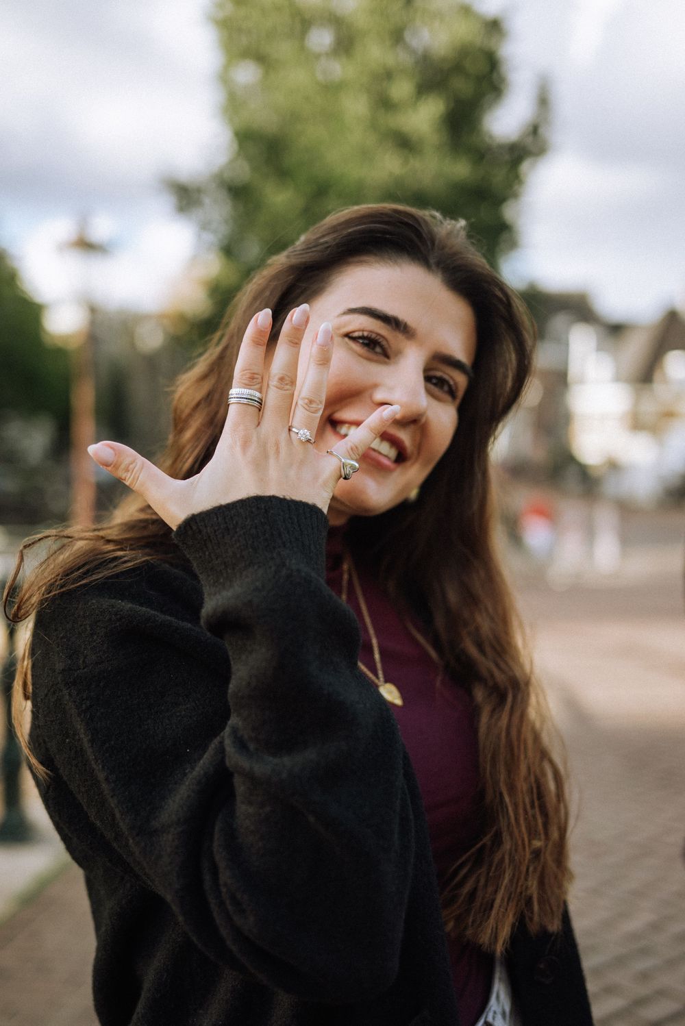 A person in a black sweater laughs joyfully outdoors.