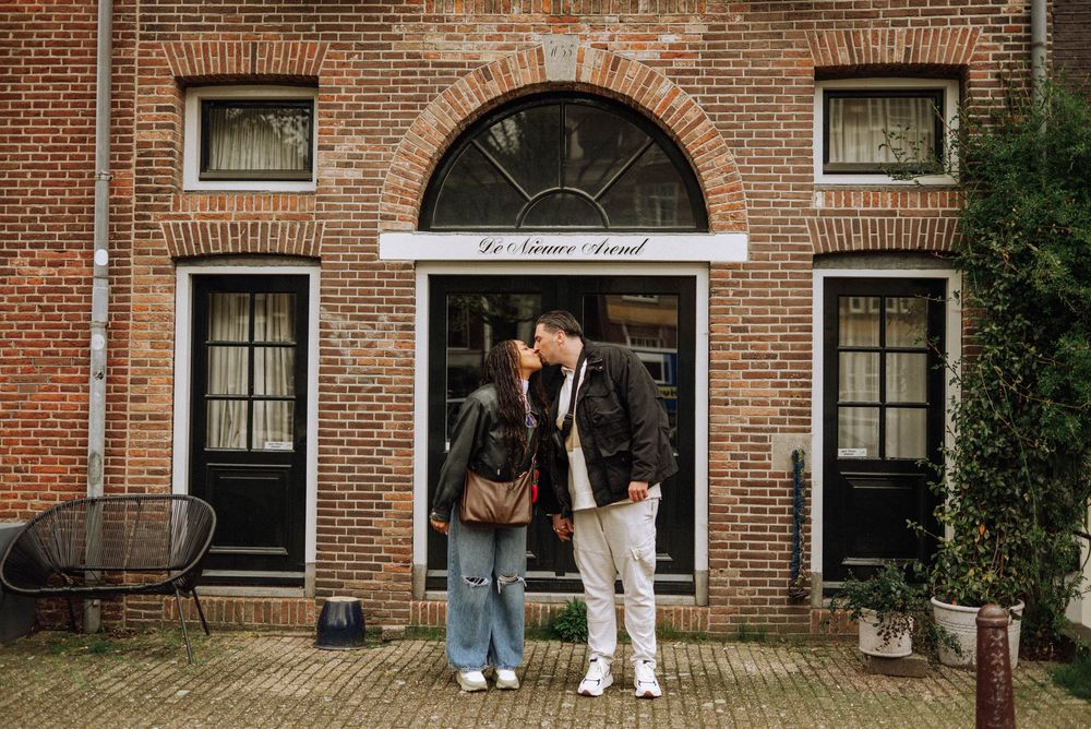 Couple sharing a kiss in front of a brick building with arched doorway in a charming European town.