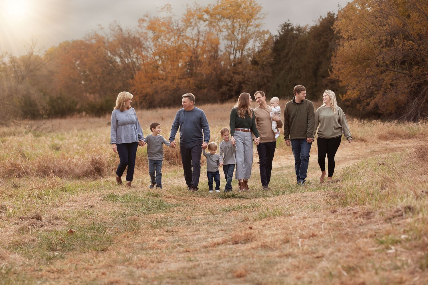 Group of people walking together along a grassy hill path during golden autumn sunset hour.