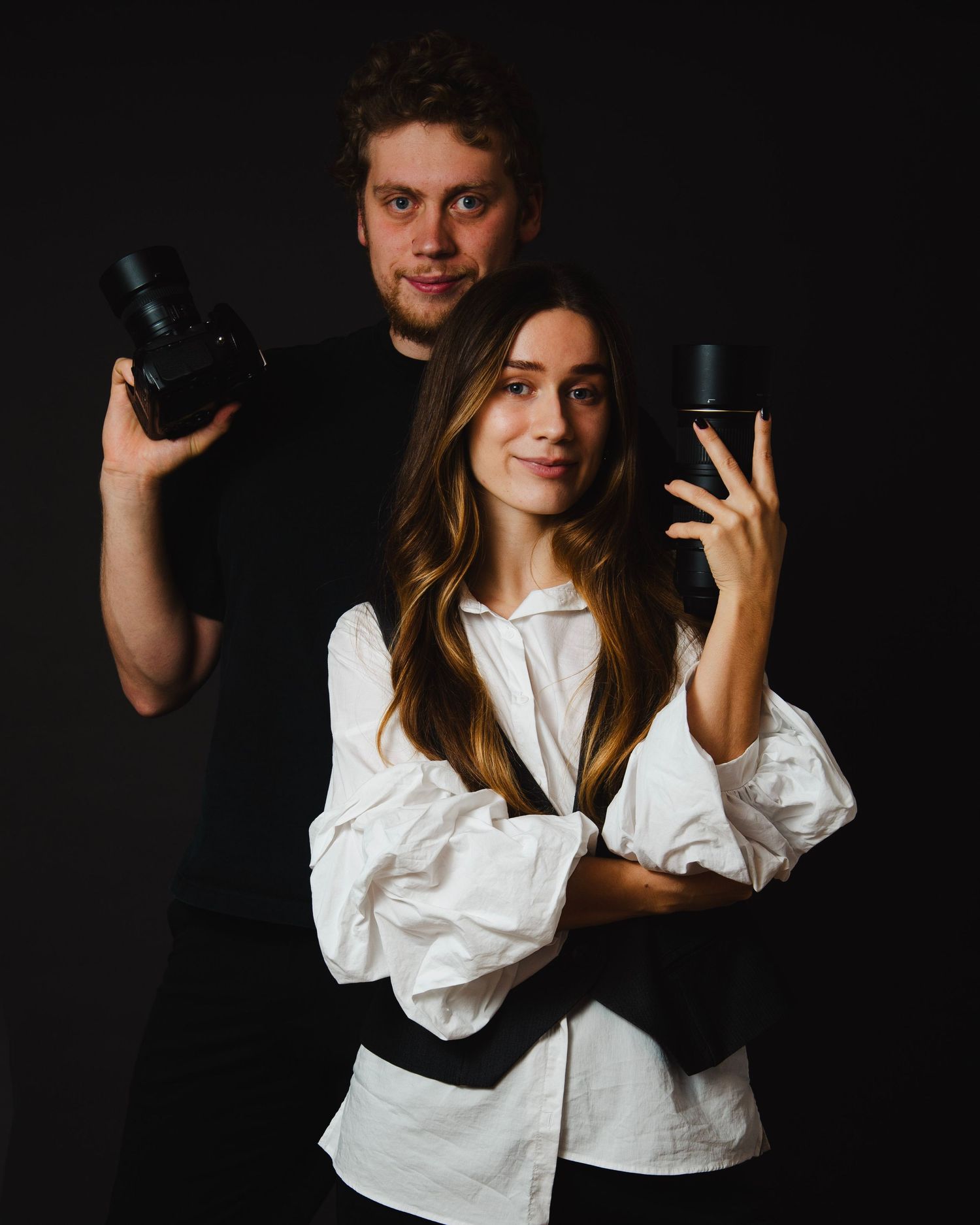 Person in white button-down shirt poses with camera against dark background in creative portrait series.