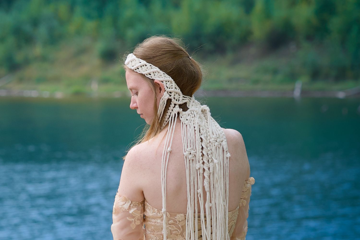 A delicate blush pink dress with lace details photographed from behind against a serene lake and forest backdrop.