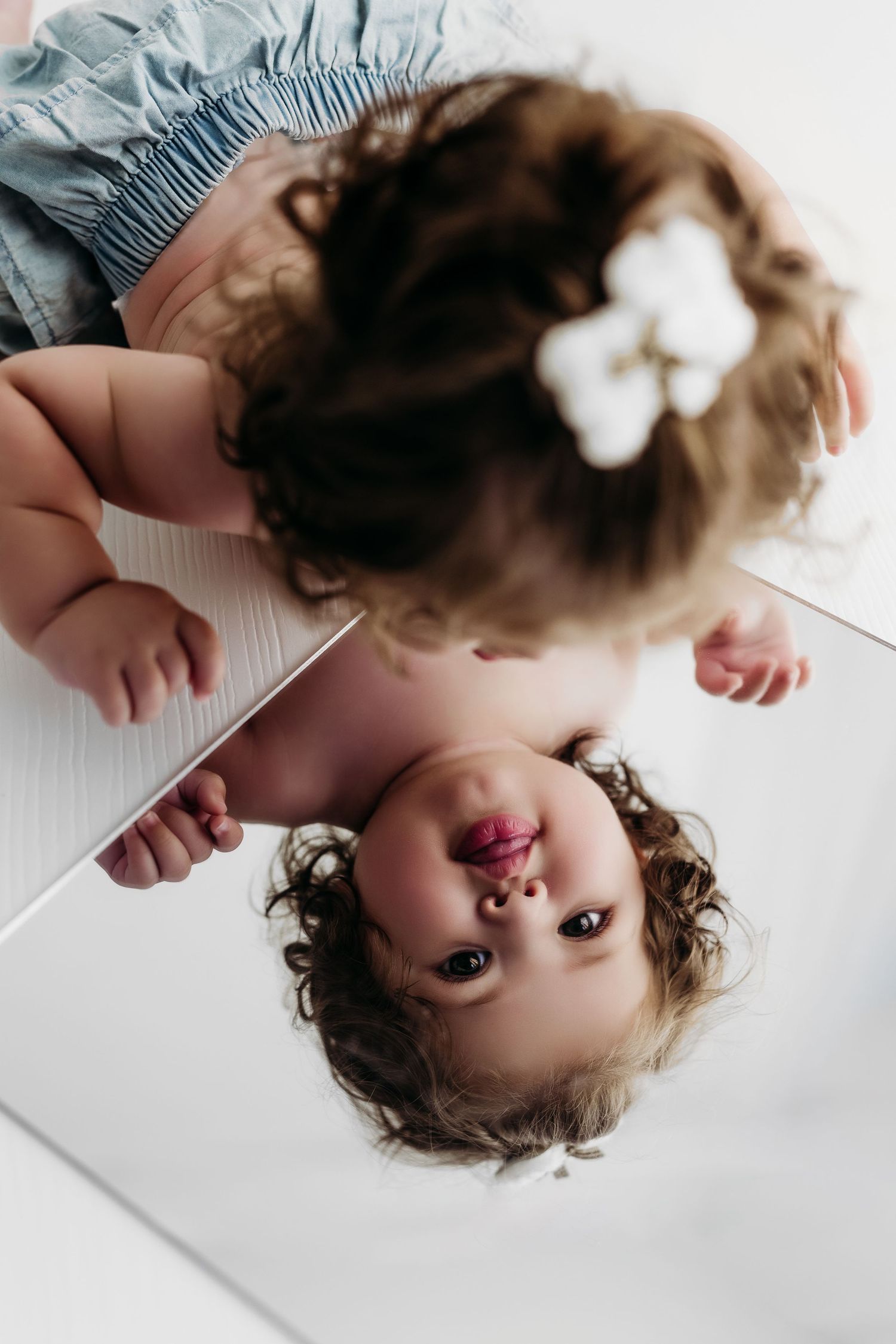 A small child in a striped romper sits on a wooden stool against a white background.