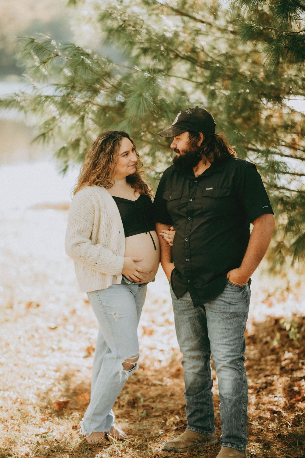 A couple shares romantic moments in a sunlit wooded area with autumn leaves scattered on the ground.
