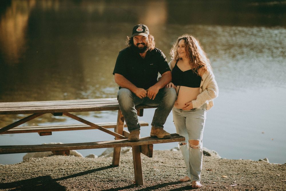 Couple sitting together on wooden dock at sunset by tranquil lake in romantic outdoor setting.