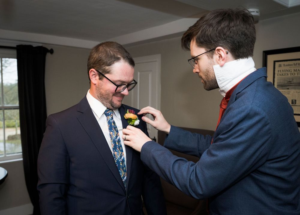 Men in formal suits help each other adjust ties and boutonnieres before the ceremony.