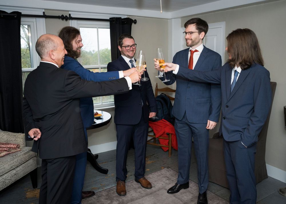 Groomsmen in navy suits gather before the wedding ceremony in a bright indoor space.