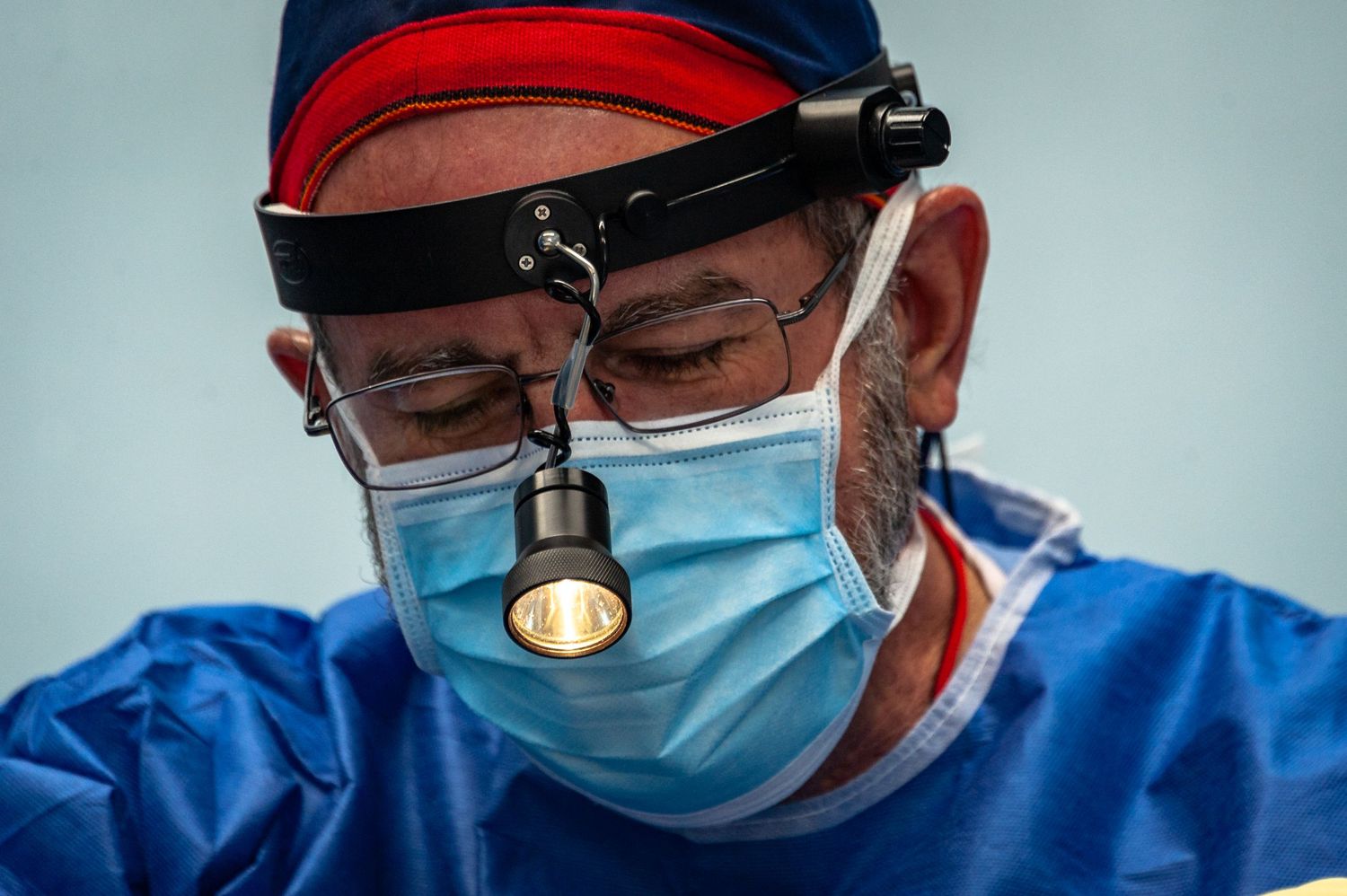 A medical professional wearing surgical mask, blue scrubs and magnifying headgear performs a detailed examination.