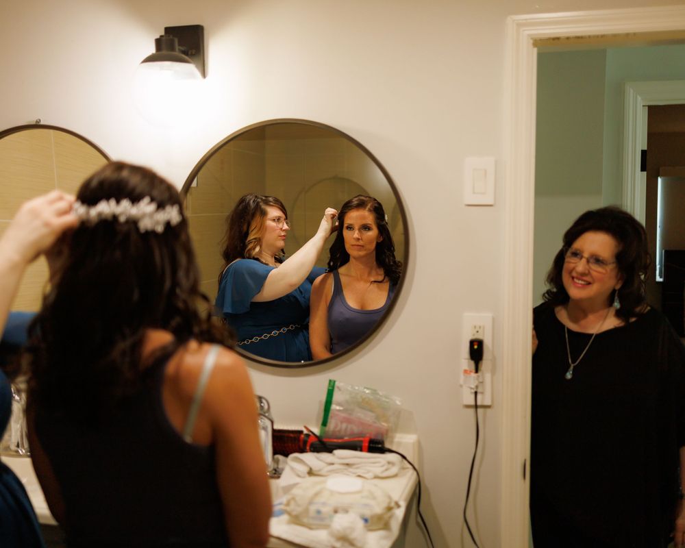 A warm reflection in the mirror shows people getting ready in a room with white walls and a wall sconce.