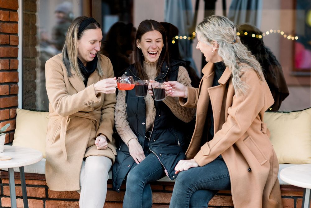 Friends enjoying drinks and conversation at an outdoor cafe with exposed brick walls.